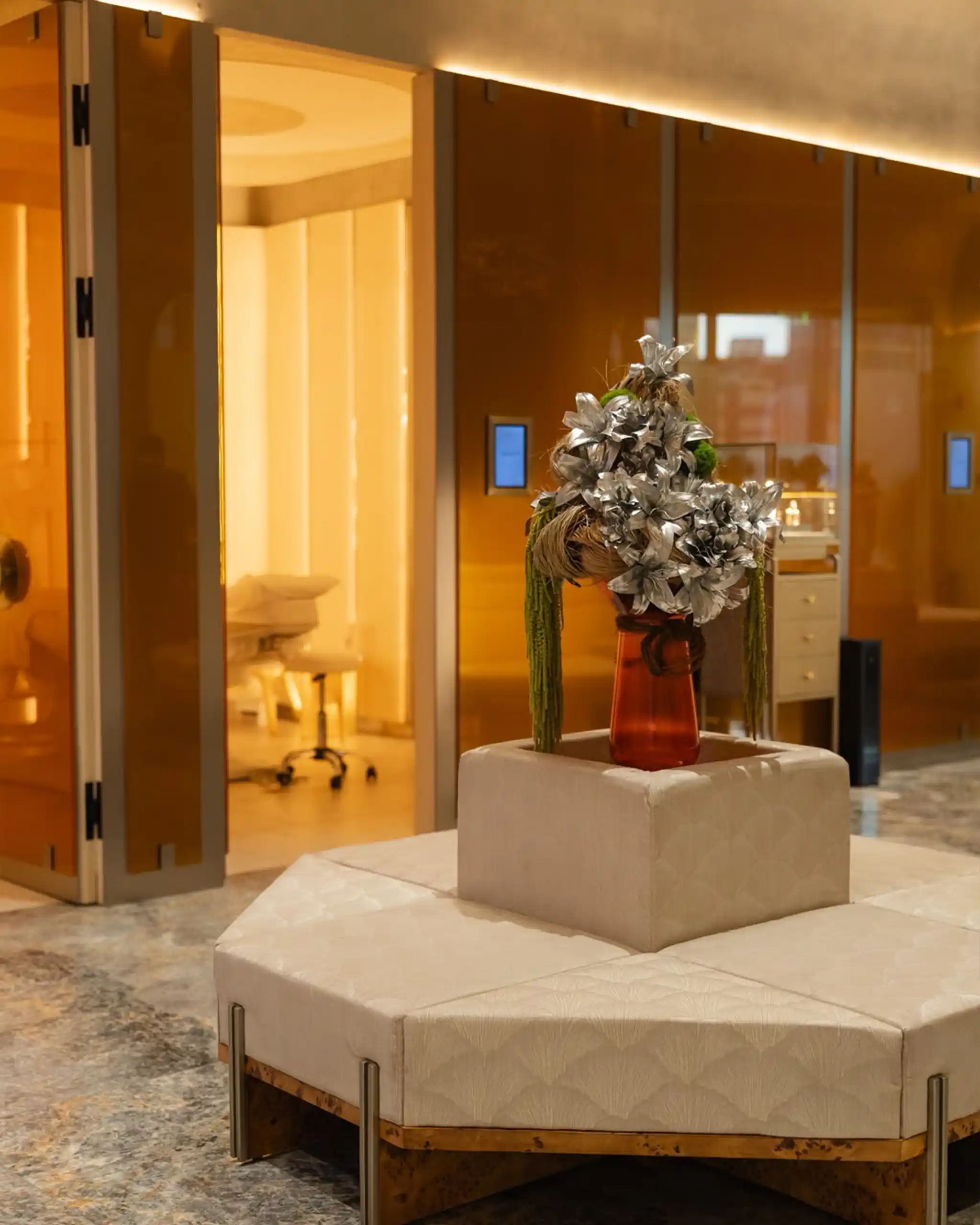 Decorative centerpiece: silver-leaf sculpture in a red vase on a white pedestal in a modern lobby setting.