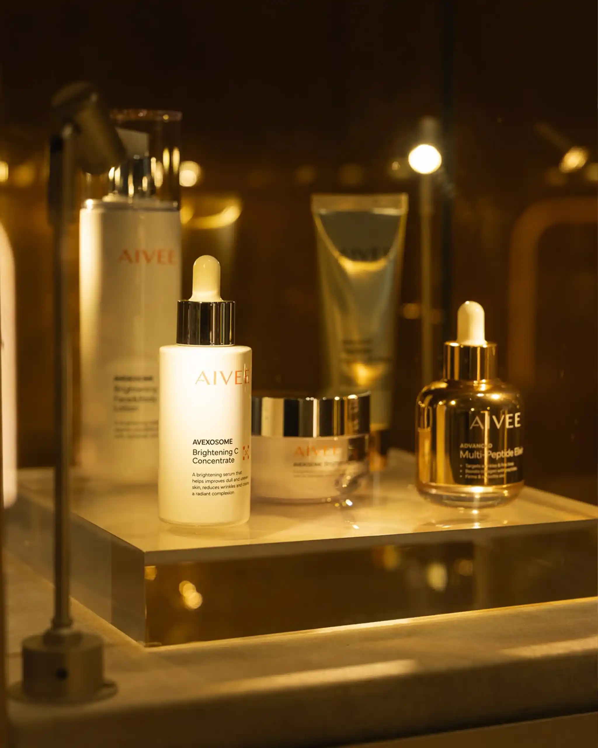 Close-up of AIVEE skincare bottles on a warm-lit bathroom shelf.