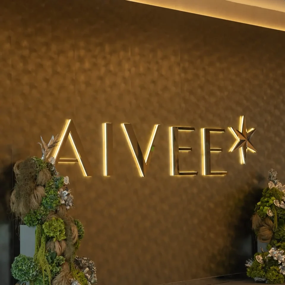 Gold-toned wall backdrop with illuminated geometric lines and lush floral arrangements on both sides.