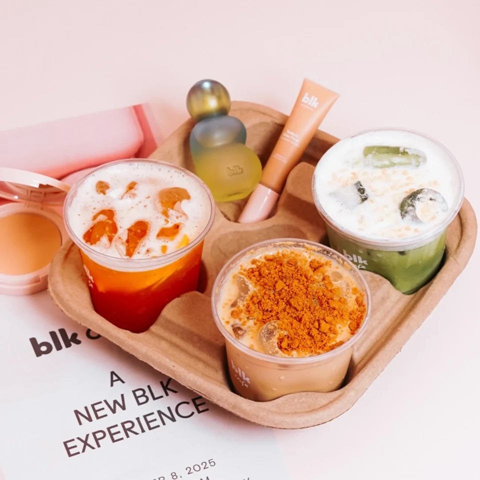 Tray of colorful beverages with toppings, on a brown tray against a pale pink background; cups show 'blk' branding