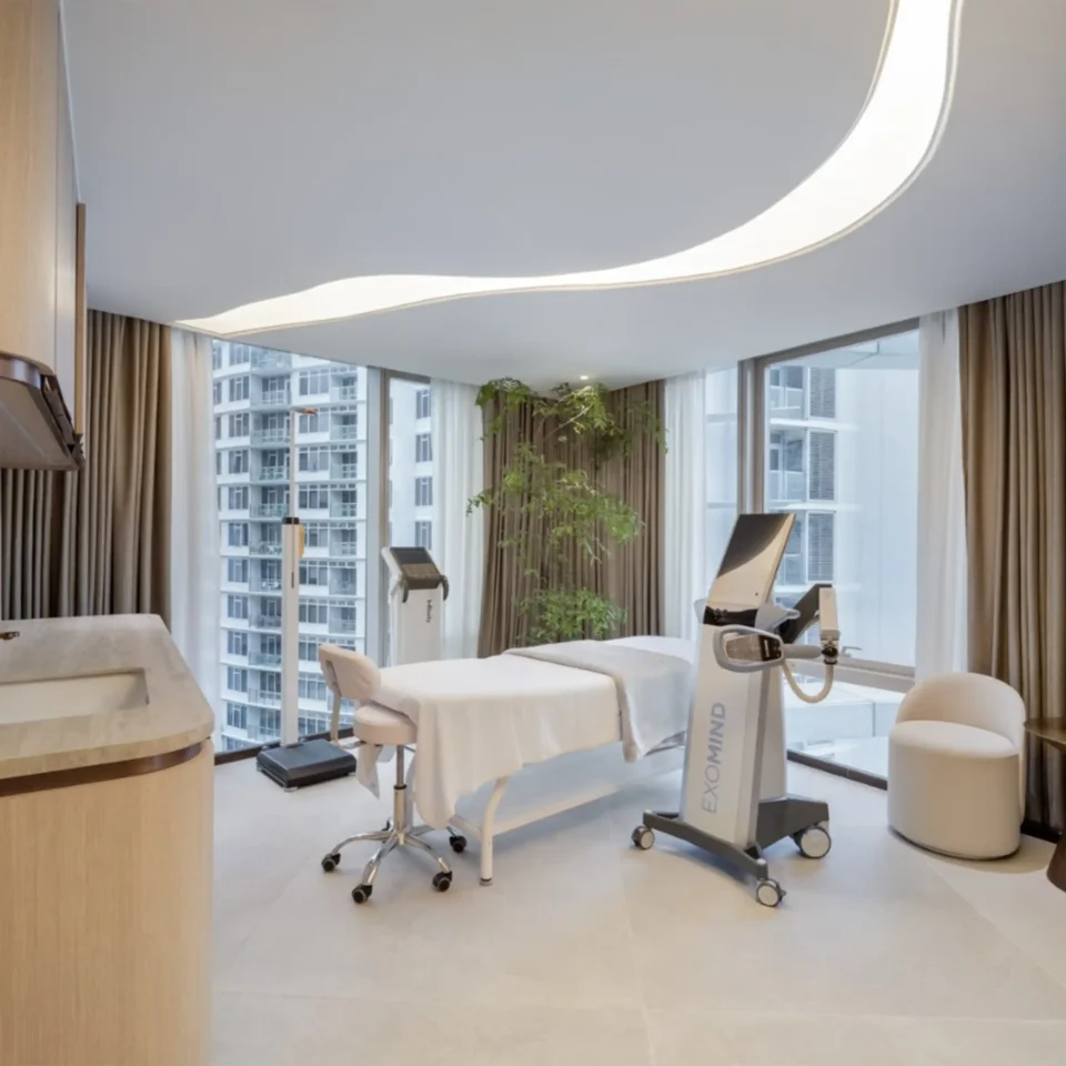 Contemporary clinic or spa treatment room with a curved white ceiling light feature, white rolling chairs, and beige curtains by large windows showing city buildings outside