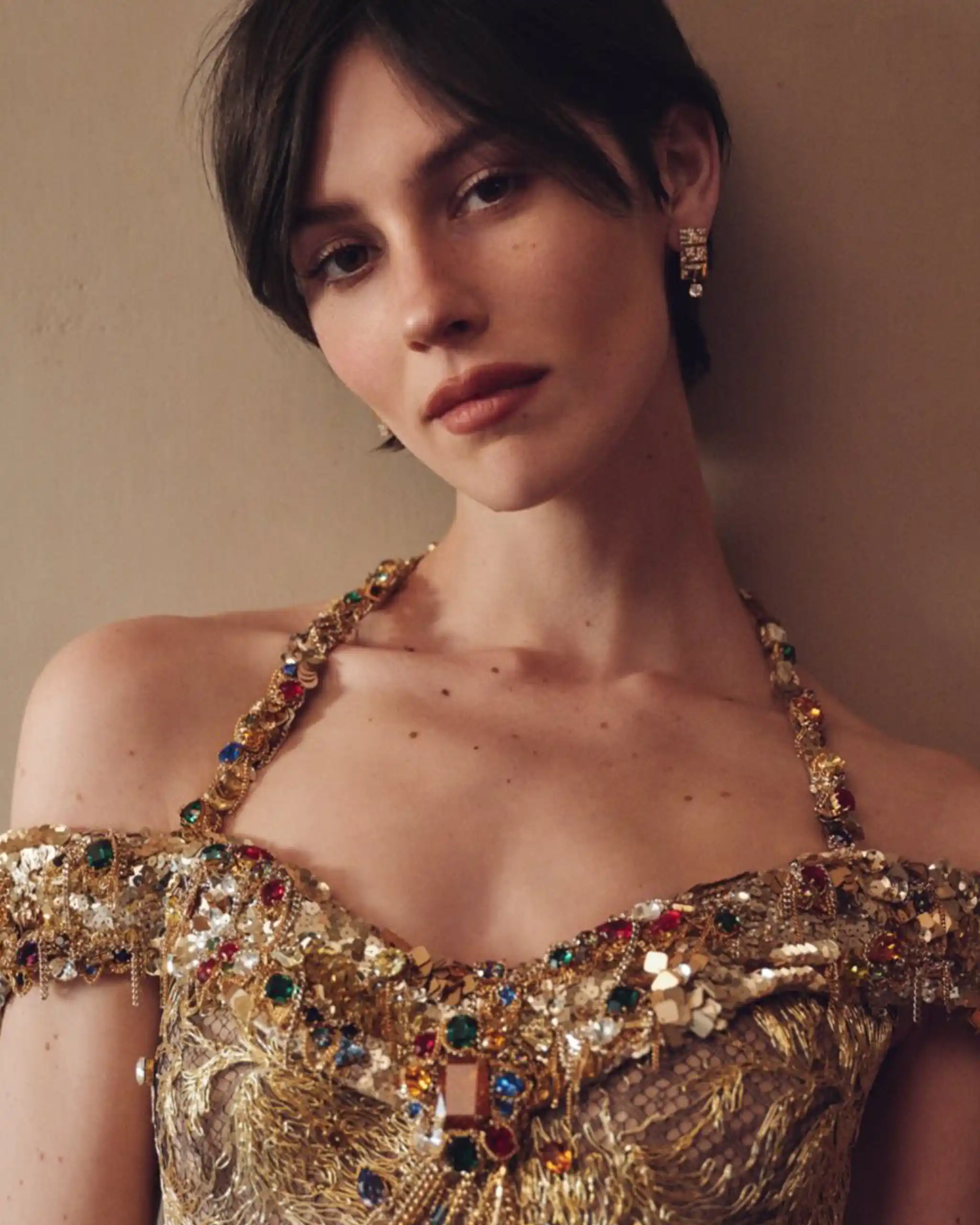 Close-up of a woman wearing a gold sequined necklace and matching earrings, in a jewel-toned evening gown.