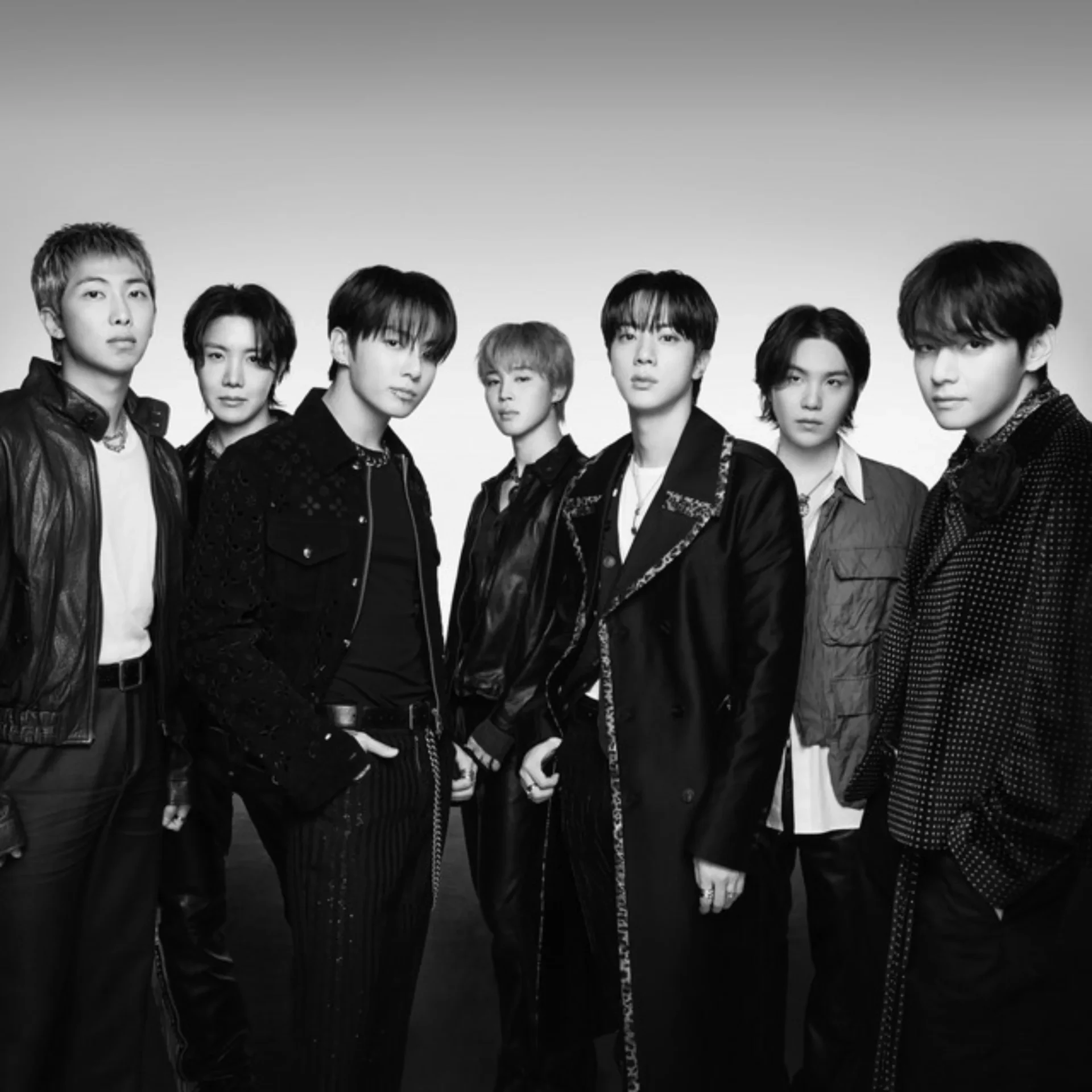 Seven men in stylish black outfits posing together in a studio photo (black and white).