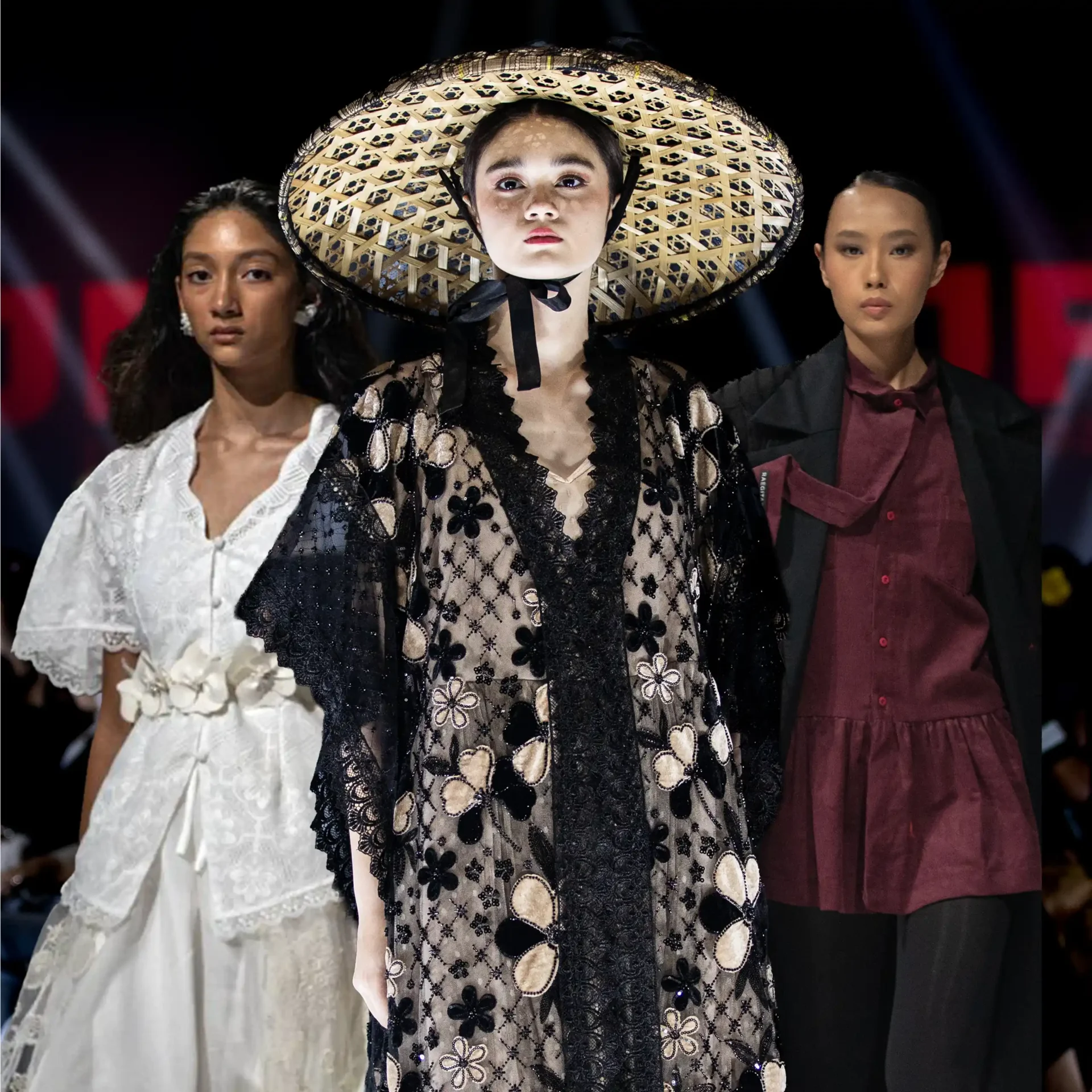 Model wearing an oversized woven straw hat and black lace dress on a runway, flanked by two other models in white and burgundy outfits.