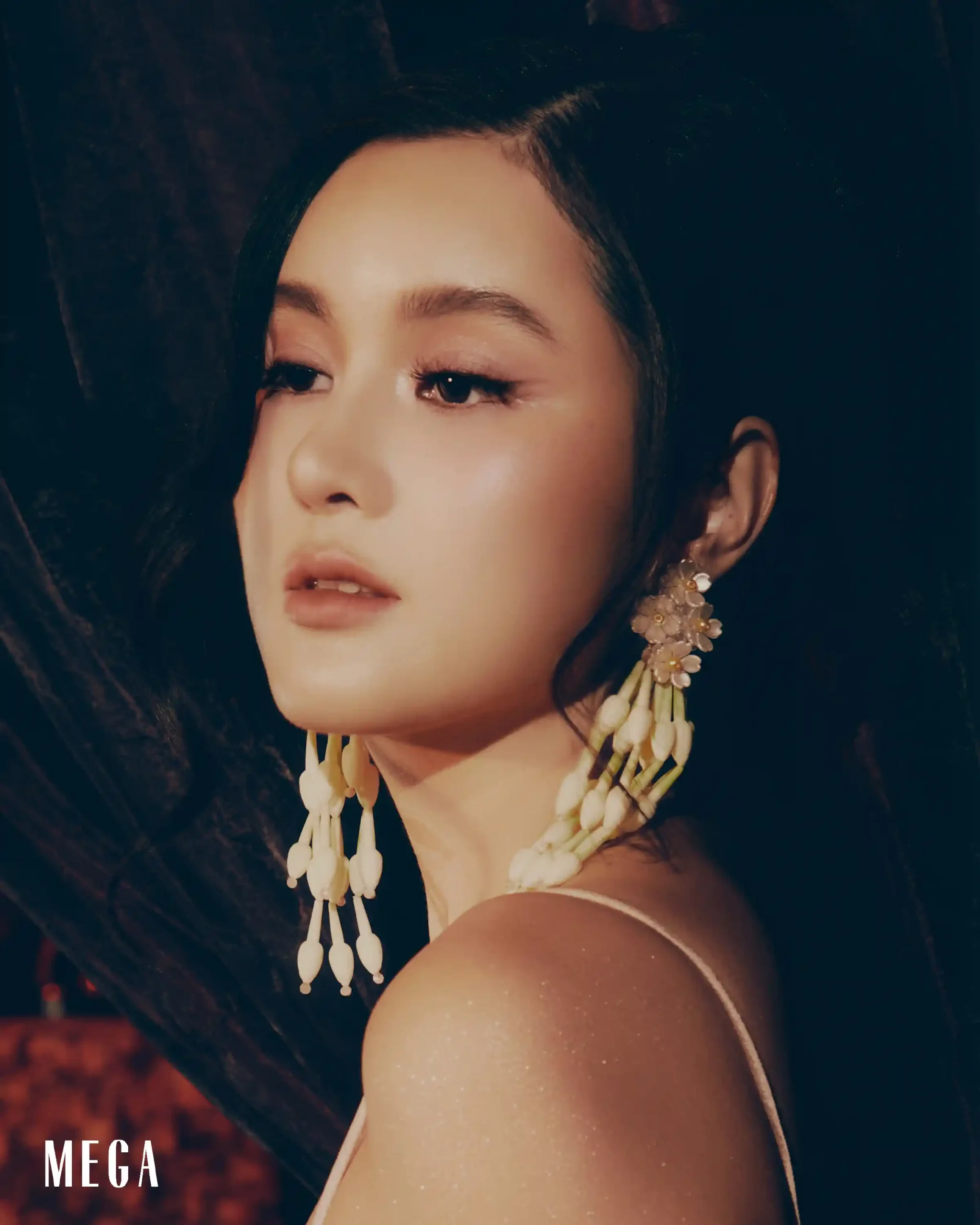 Close-up side profile of a woman with subtle pink makeup, wearing large white floral earrings.
