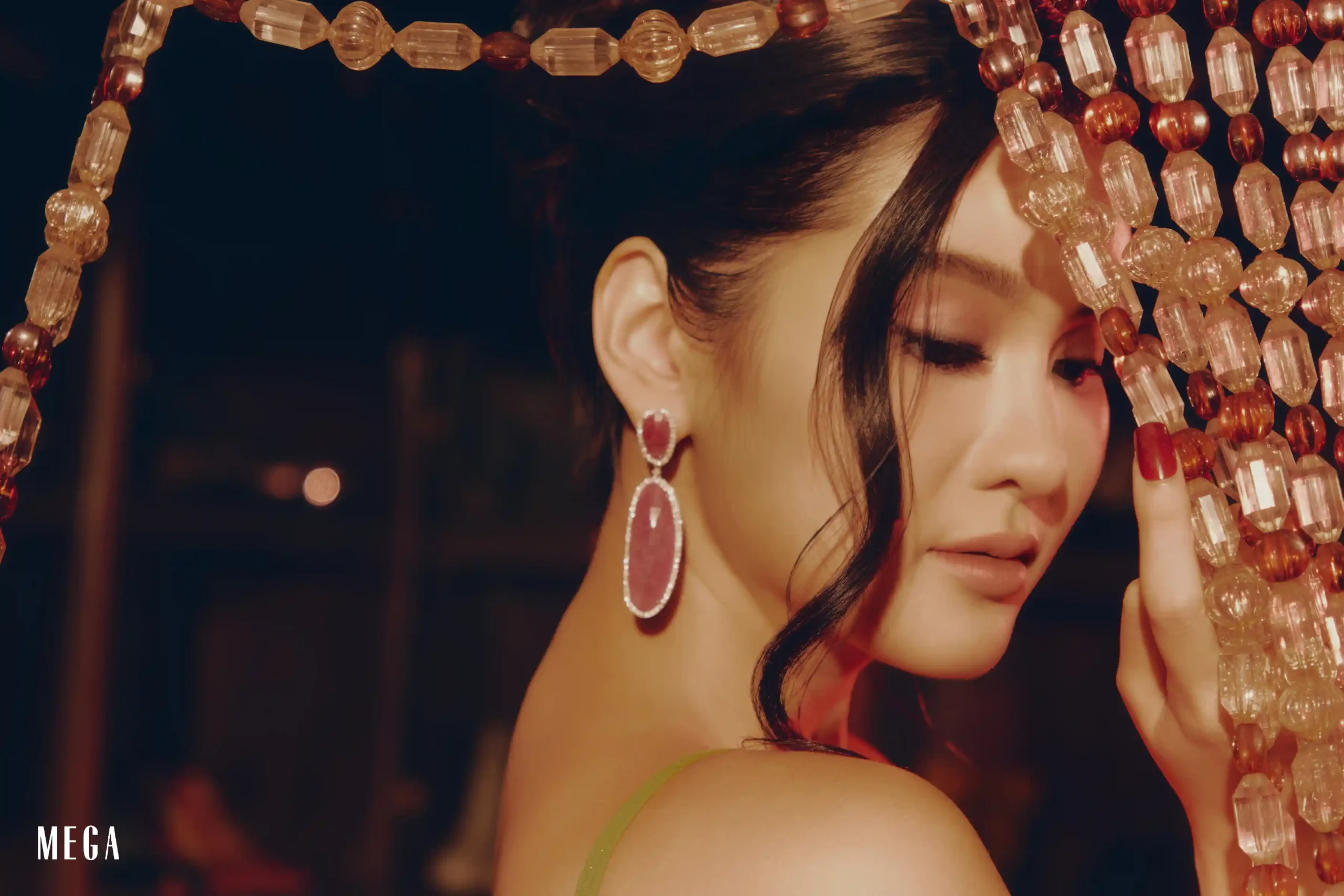 Close-up portrait of a woman with pink gemstone earrings, framed by pink and clear bead strands cascading around her face.