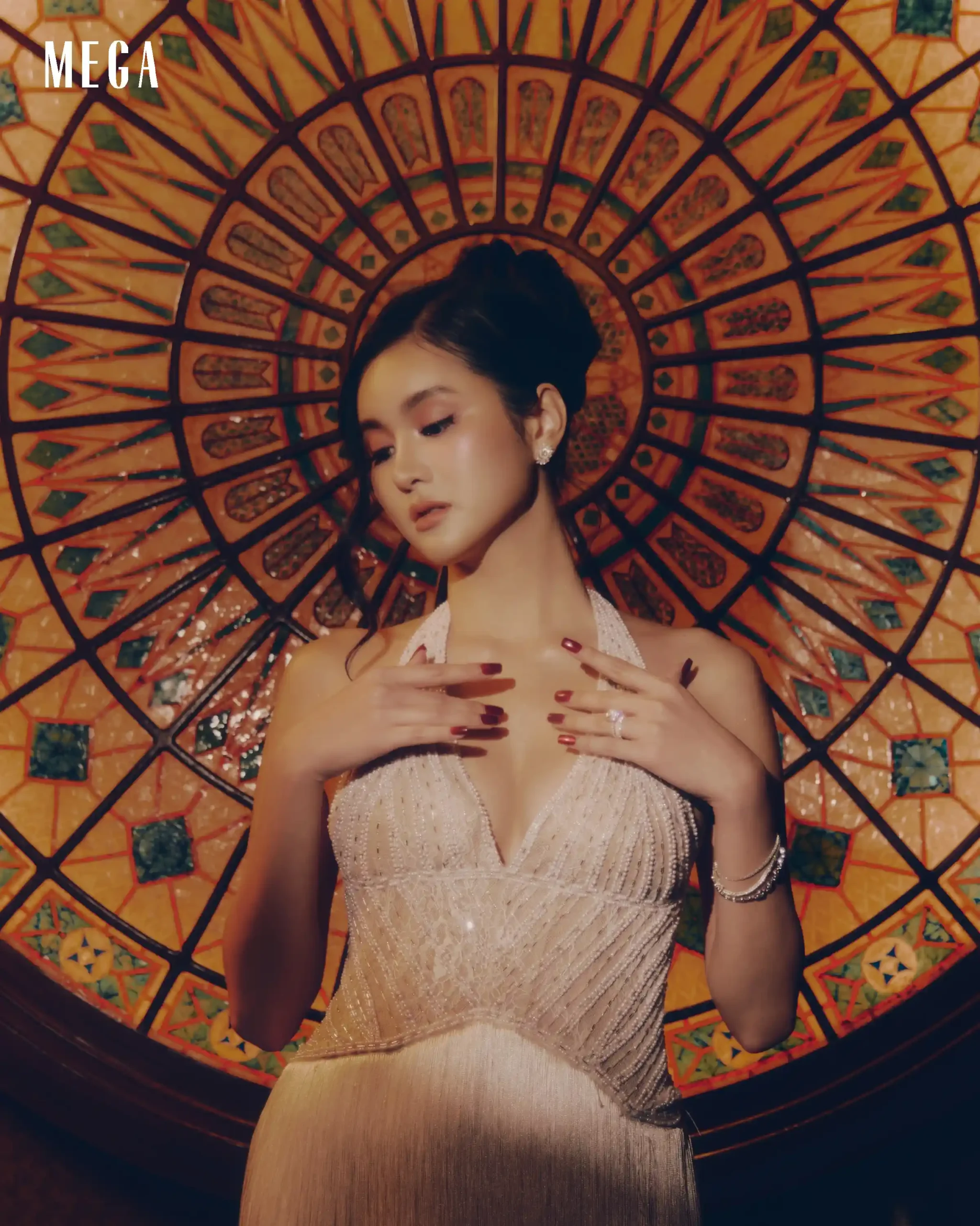 Portrait of a woman in a glittering silver dress posed in front of a large orange and green mosaic parasol.