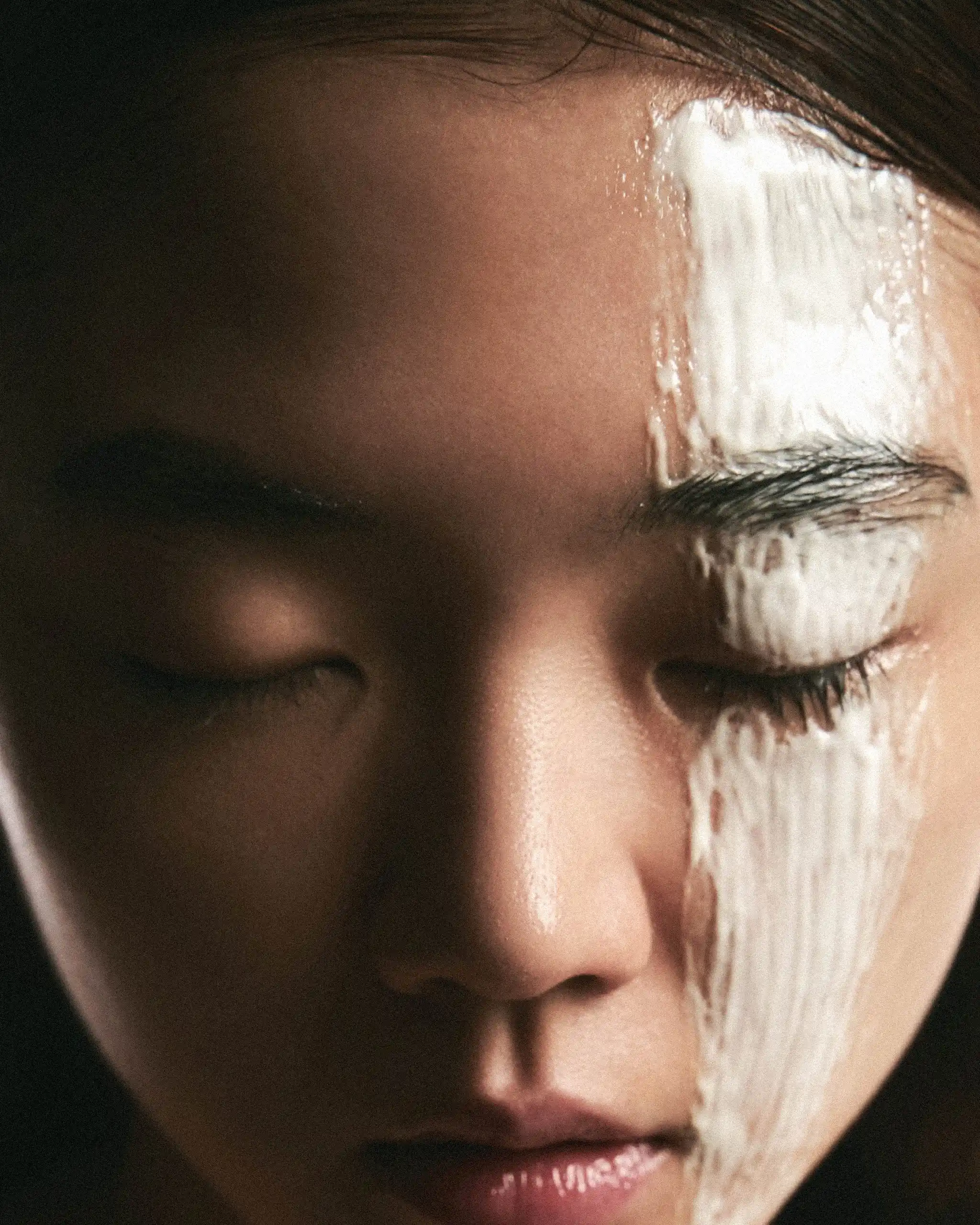 Close-up of a person's face with white facial cream on the eyelid and brow, eyes closed.