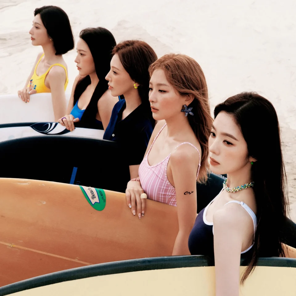 Four young women in swimsuits leaning on a large orange surfboard on a boat.