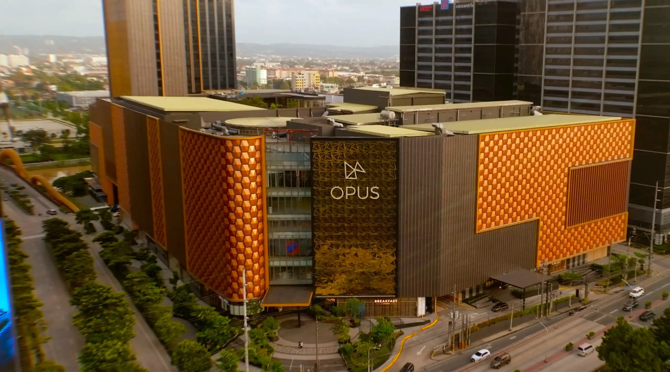 Aerial view of the OPUS building with orange geometric panels and dark vertical façade in a cityscape.