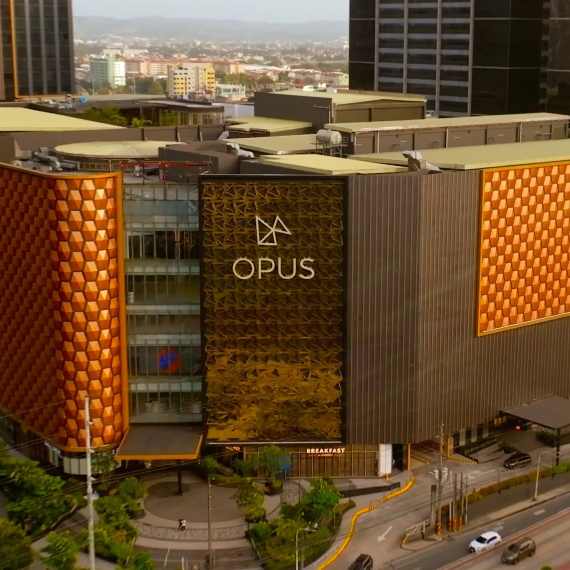 Aerial view of a city block with the orange geometric OPUS building facade and nearby roads and plaza below.