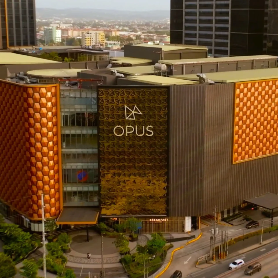 Aerial view of a city block with the orange geometric OPUS building facade and nearby roads and plaza below.