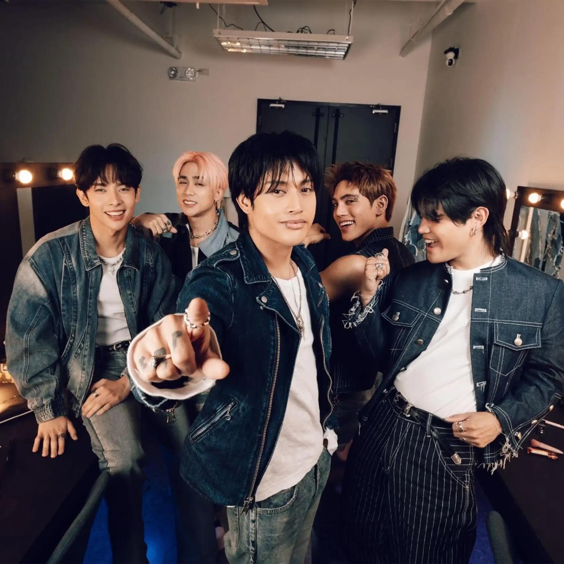 Group of young men in denim jackets posing together in a backstage dressing room for a selfie/photo shoot.