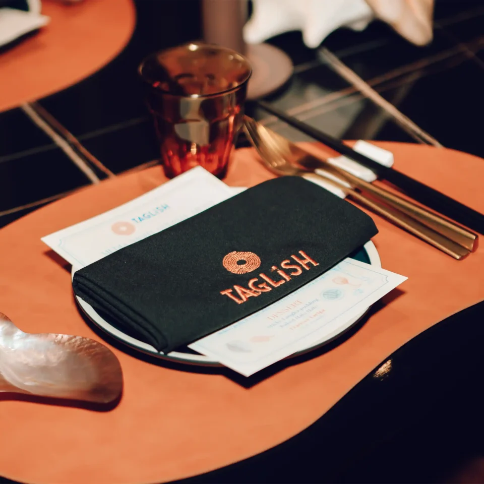 Close-up of a ruby-colored glass on an orange table beside a black notebook and scattered papers.