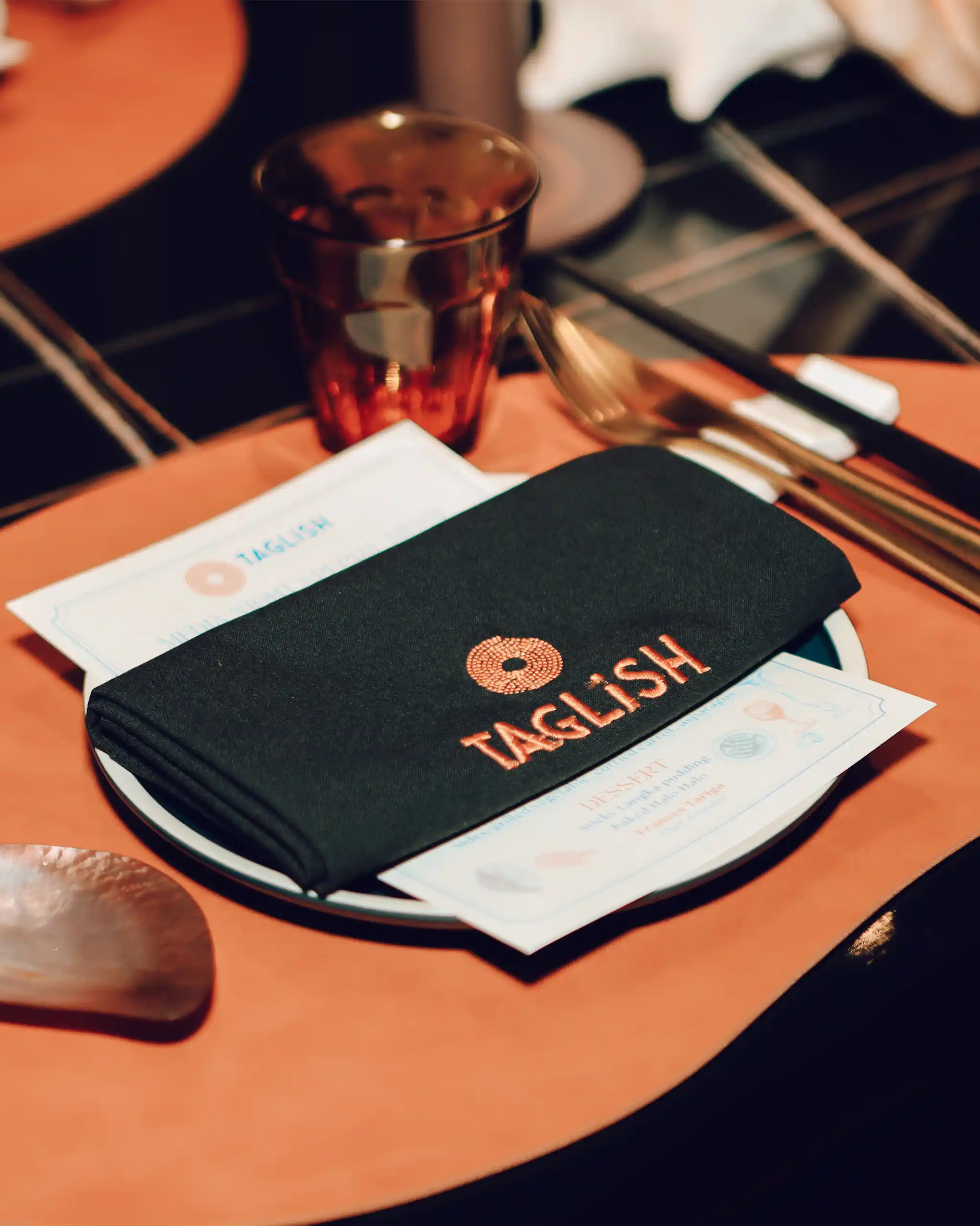 Close-up of a metallic copper cup on an orange table, with a dark wallet and scattered papers nearby.