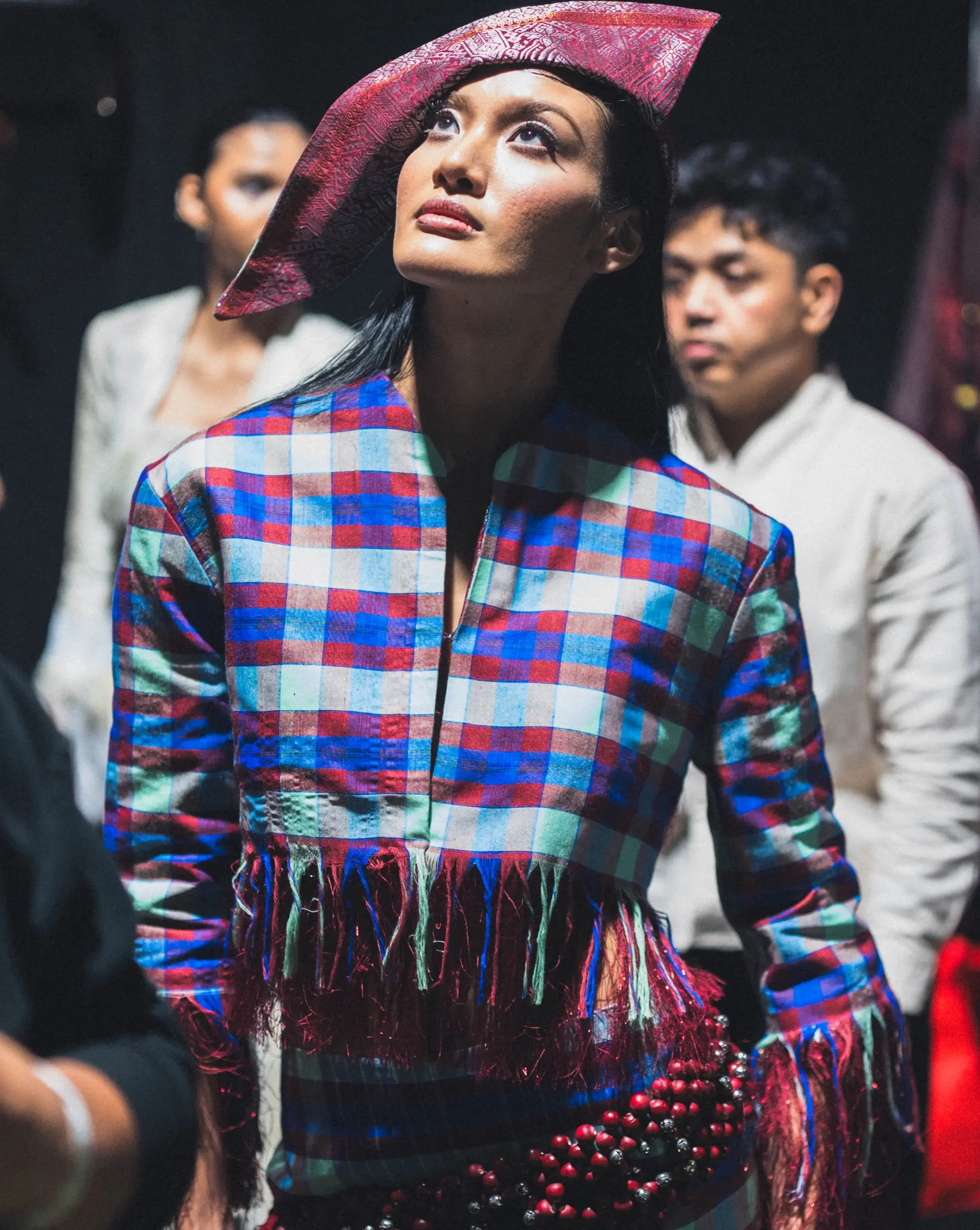 Model wearing a bright plaid jacket and red patterned hat, looking upward at a fashion show